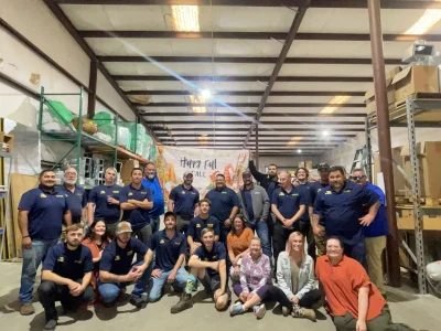 Large group of Southern Air Acadiana employees posing together in a warehouse with a Happy Fall banner visible in the background.