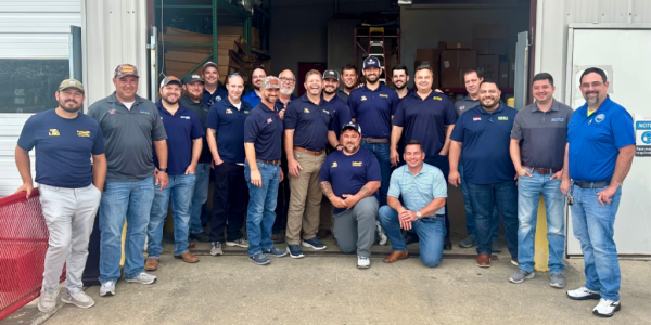 Professional team of HVAC, plumbing, and electrical service technicians posing together outside a warehouse facility in Baton Rouge.
