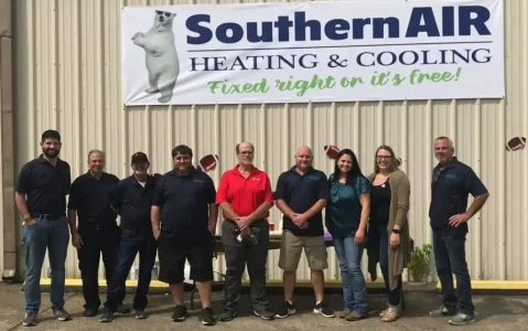 Team of ten employees standing in front of Southern AIR Heating & Cooling building with company logo and tagline visible.