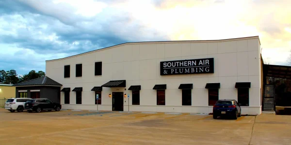 Modern commercial building with white facade and black awnings displaying Southern Air & Plumbing signage, with parking lot and vehicles.